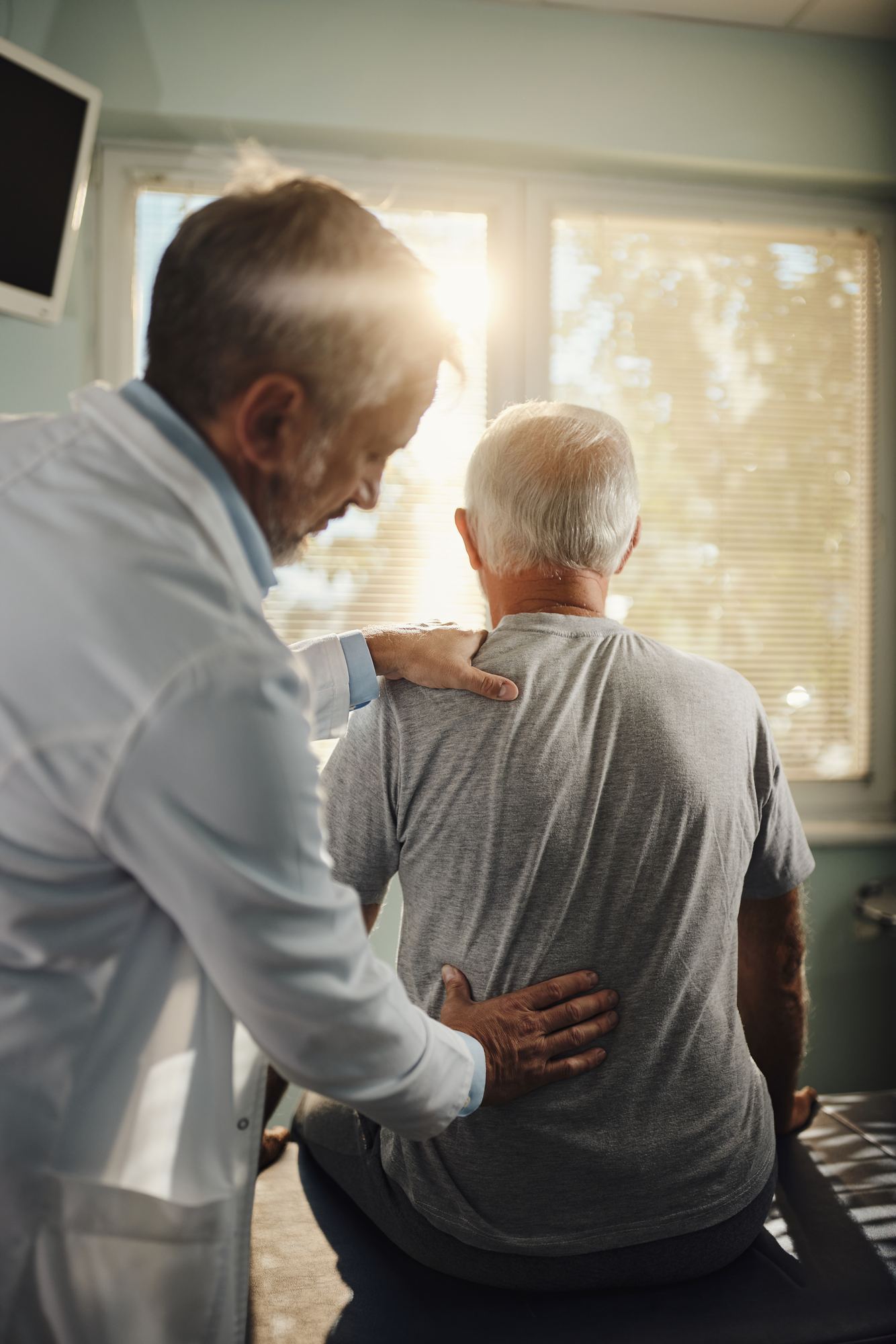 Doctor examining an older man's back
